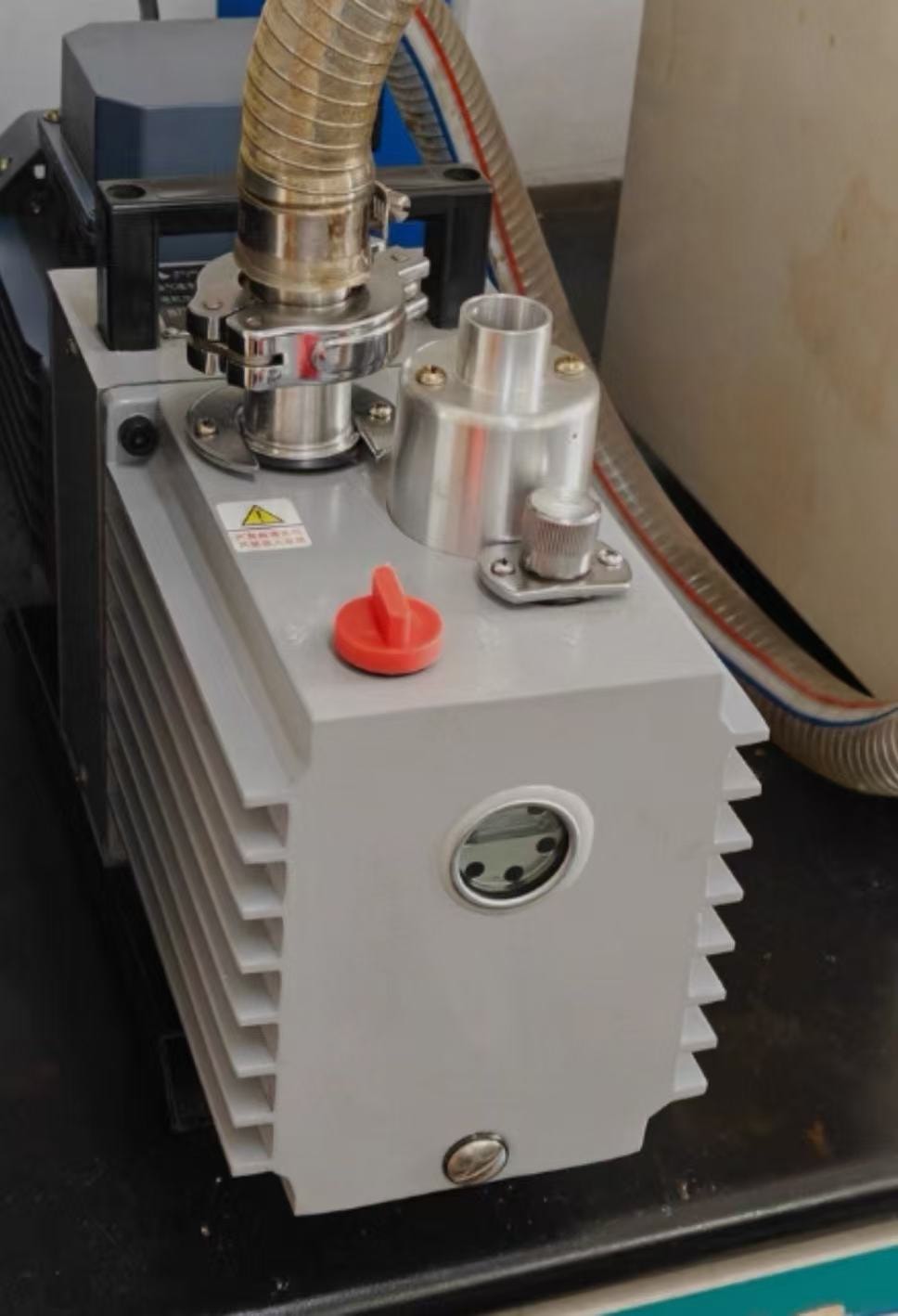 Rotary vane vacuum pump connected to industrial process equipment through a vacuum hose